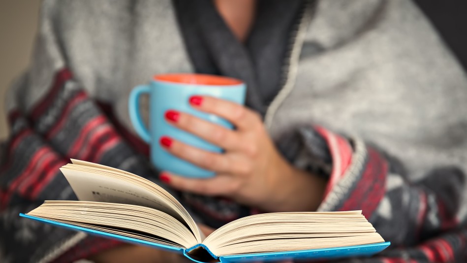 Une femme, aux ongles vernis de rouge, lit avec une tasse de café dans ses mains
