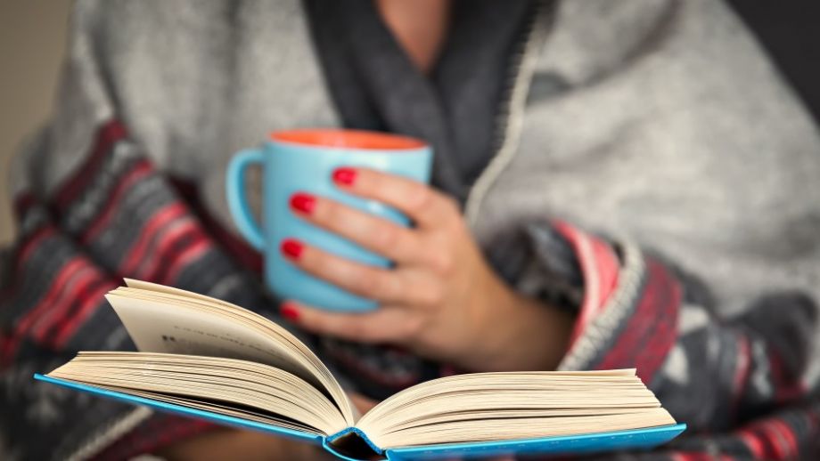 Une femme, aux ongles vernis de rouge, lit avec une tasse de café dans ses mains