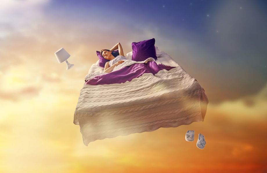 Une femme endormie dans son lit rêve en volant dans les nuages.